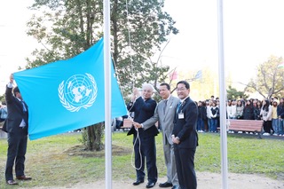 東日本国際大学キャンパスで行われた国連旗掲揚式。CIFALジャパンの代表者と国連ユニタール人々・社会包摂部長のアレックス・メヒア氏が国連旗を掲揚し、学生が見守る様子。